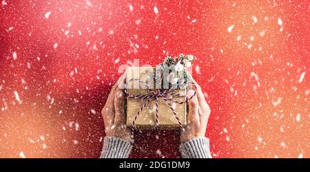 Papier-Geschenkbox mit Schleife in Damen Hände auf rotem Hintergrund in abstrakten Schneefall. Stockfoto