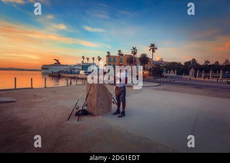 Angeln neben einem Neptunbrunnen mit Castillo De Los Tres Reyes del Morro im Hintergrund das Schloss, Malecon/Avenida del Puerto, Havanna, Kuba Stockfoto