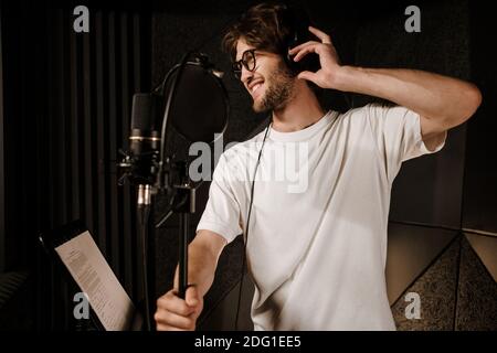 Junge attraktive männliche Sänger glücklich hören Klang in Kopfhörer Vorbereitung Nehmen Sie den Song im Studio auf Stockfoto