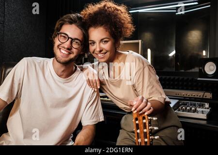 Junge fröhliche Musiker, die fröhlich in die Kamera schauen und neue Songs aufnehmen Zusammen in einem modernen Studio Stockfoto