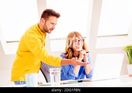 Aufnahme einer Geschäftsfrau mittleren Alters, die am Laptop arbeitet, während ihr Kollege neben ihr steht und etwas auf dem Laptop-Bildschirm zeigt. Teamarbeit Stockfoto