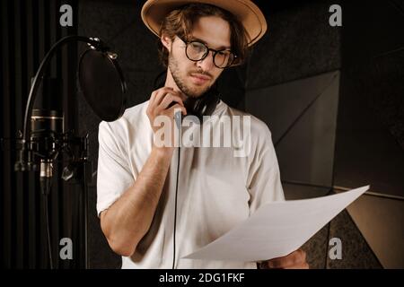 Junge selbstbewusste männliche Sängerin nachdenklich lesen Text des neuen Songs Arbeiten im Tonstudio Stockfoto