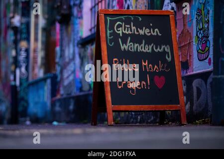 Köln, Deutschland. Dezember 2020. 'Glühwein Wanderung - bitte Maske tragen!' Steht auf einem Brett vor einem Verein in Ehrenfeld. Nach Berichten über Verstöße gegen die Corona-Regeln bei Glühweinwanderungen hat das Gesundheitsministerium die öffentlichen Ordnungsbehörden aufgefordert, einheitliche Kontrollen durchzuführen. Wo nötig, sollten Geldstrafen und Verbote verhängt werden, teilte das Ministerium der Deutschen Presseagentur auf Antrag mit. Quelle: Rolf Vennenbernd/dpa/Alamy Live News Stockfoto
