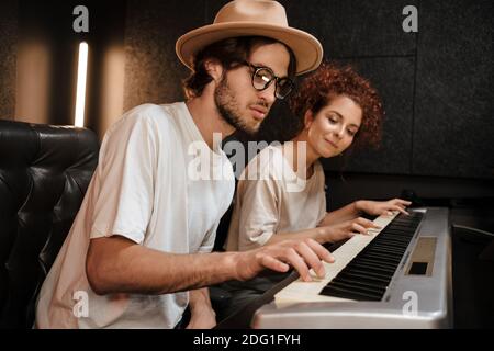 Junge stilvolle paar Musiker traumartig komponieren Musik auf Klavier Keyboard arbeitet im modernen Aufnahmestudio zusammen Stockfoto