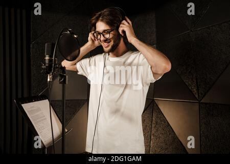 Attraktive lächelnde Kerl glücklich trägt Kopfhörer Aufnahme neuer Song in Modernes Studio Stockfoto