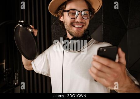 Portrait von schönen stilvollen männlichen Sänger mit Smartphone Aufnahme neu Lied im Tonstudio Stockfoto