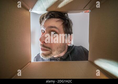 Junger neugieriger und verdächtiger Mann schaut in den Karton. Stockfoto