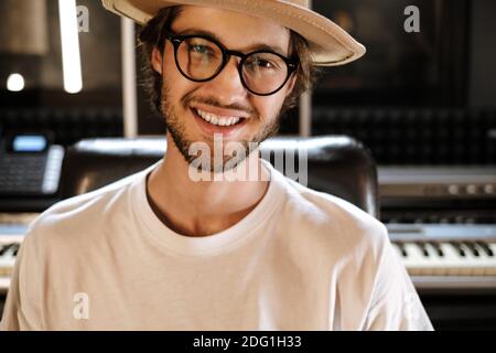 Junger stilvoller Tonproduzent, der im modernen Tonstudio arbeitet. Gutaussehender Musiker, der im Studio fröhlich in die Kamera schaut Stockfoto