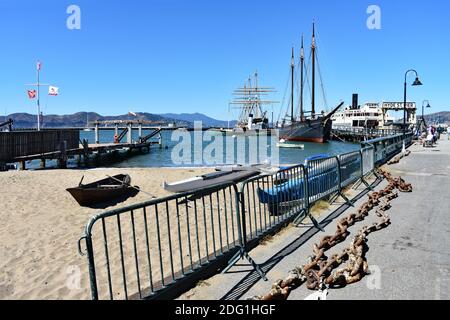 Hyde Street Pier, Teil des San Fransisco Maritime National Historic Park. Ein Strand mit kleinen Booten auf und größere Schiffe sind am Pier vertäut. Stockfoto