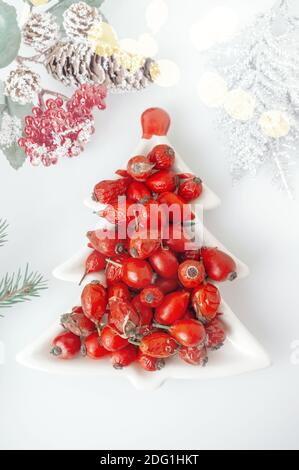 Hagebutte Beeren in einer Porzellanschale in Form eines Weihnachtsbaums auf einem hellen Hintergrund Nahaufnahme. Beeren für die Herstellung von Vitamin-Tee oder trinken auf kalt w Stockfoto