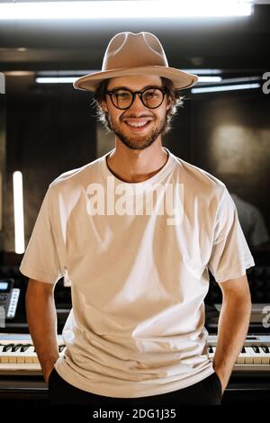 Gut aussehende zuversichtlich Kerl in Hut glücklich Blick in der Kamera im Studio. Junger stilvoller Tonproduzent, der im Aufnahmestudio arbeitet Stockfoto