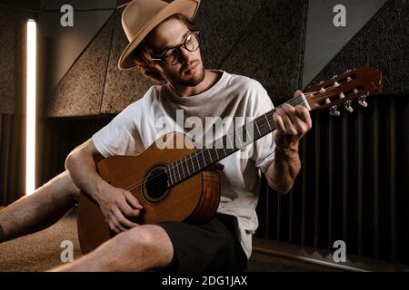 Junger attraktiver männlicher Musiker spielt nachdenklich auf der Gitarre im Tonstudio. Hübscher Kerl, der Song im Studio komponiert Stockfoto