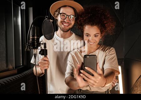 Ein paar attraktive stilvolle Sänger nehmen gerne Selfie zusammen auf Smartphone im Tonstudio Stockfoto