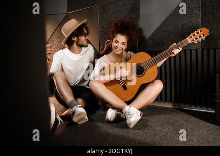 Junge attraktive Mann und Frau glücklich spielen neue Lied auf Gitarre sitzt auf dem Boden im Tonstudio Stockfoto