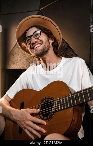 Schöner lächelnder männlicher Musiker, der freudig auf der Gitarre neues Lied spielt Im Aufnahmestudio Stockfoto