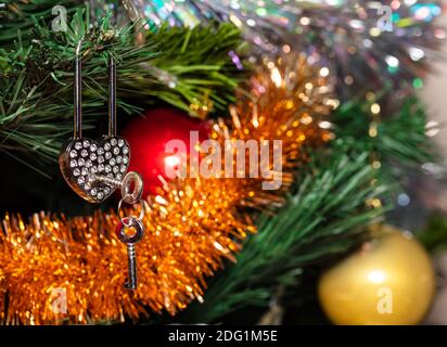 Herzschloss aus Metall mit Schlüssel am Weihnachtsbaum. Nahaufnahme. Rote, goldene Kugeln und weiße und goldene Lametta verschwommen im Hintergrund Stockfoto