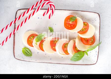 Weihnachten Caprese Salat in Form von Candy Cane, Mozzarella und Tomaten auf dem Teller serviert für Neujahr und Weihnachten, mit Weihnachtsdekor auf weißer Tischplatte Stockfoto