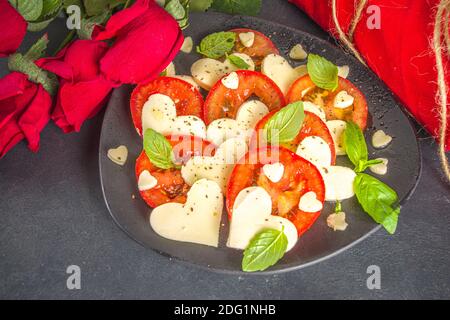 Caprese Salat zum Valentinstag Abendessen, mit Tomaten, Käse in Form von Herzen, Basilikum. Valentine day Menü Konzept Draufsicht Kopieplatz Stockfoto