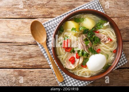 Südamerikanische Caldo de Gallina Hühnernudelsuppe mit gekochtem Ei und Kräutern aus der Nähe auf einem Teller auf dem Tisch. Horizontale Ansicht von oben Stockfoto