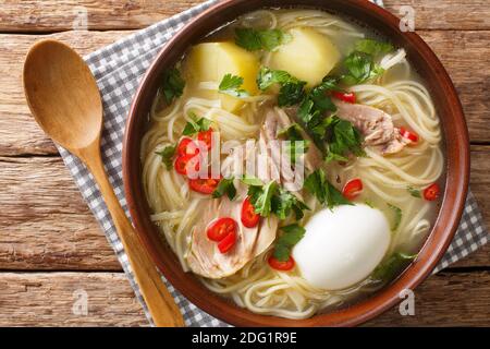 Peruanische Caldo de Gallina Hühnersuppe aus der Nähe in der Platte auf dem Tisch. Horizontale Draufsicht von oben Stockfoto