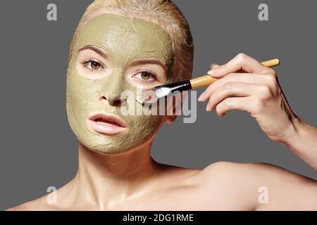 Schöne Frau, Die Grüne Gesichtsmaske Anwendet. Schönheitsbehandlungen. Close-up Portrait of Spa Girl Tragen Sie Clay Gesichtsmaske auf grauem Hintergrund. Stockfoto