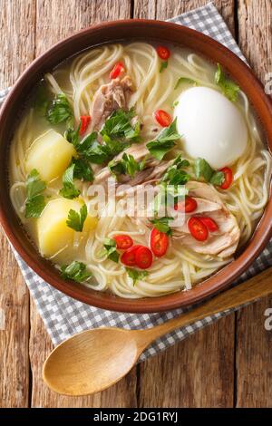 Peruanische Caldo de gallina Hühnernudel-Suppe aus der Nähe in einem Teller auf dem Tisch. Vertikale Ansicht von oben Stockfoto