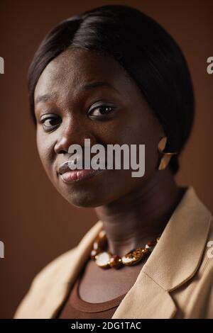 Vertikale Nahaufnahme Porträt der eleganten afroamerikanischen Frau posiert gegen Brauner Hintergrund im Studio und Blick auf die Kamera Stockfoto
