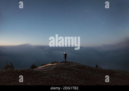 Person, die während des auf dem Berg über den Wolken steht Nacht Stockfoto