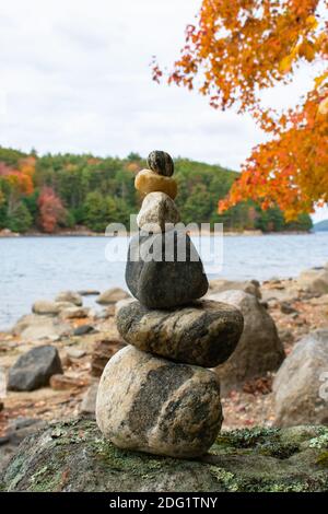 Ein Steinkairn balanciert unter Herbstlaub am Strand am See Stockfoto