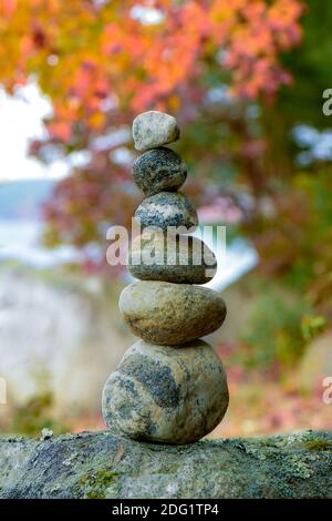 Ein Steinkairn balanciert unter Herbstlaub am Strand am See Stockfoto