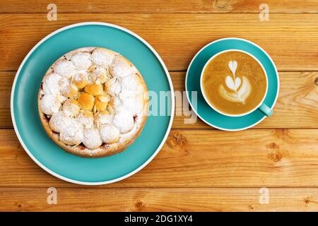 Hausgemachter Kirschkuchen mit Mandelblüten und Tasse Kaffee Cappuccino auf Holztisch. Draufsicht. Stockfoto