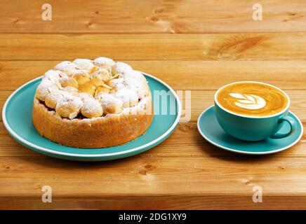 Hausgemachter Kirschkuchen mit Mandelblüten und Tasse Kaffee Cappuccino auf Holztisch. Stockfoto