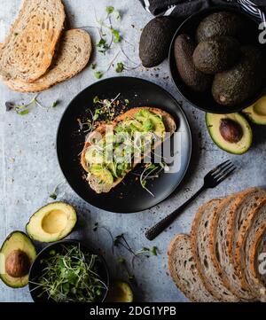 Avocado Toast auf einem Teller mit Zutaten um ihn herum auf Stein Zähler. Stockfoto