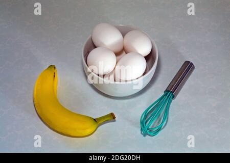 Frische Eier, ein Rührgerät, eine Banane und eine Eieruhr, um ein gesundes Frühstück vorzubereiten. Stockfoto