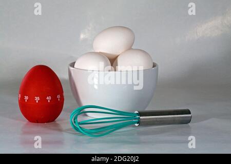 Frische Eier, ein Rührgerät und eine Eieruhr, um ein gesundes Frühstück vorzubereiten. Stockfoto