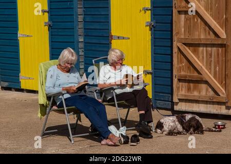 Genießen Sie die Sonne und lesen Sie in einem Liegestuhl vor einer Strandhütte an der Küste von Kent in der Nähe von Margate, Thanet, England Stockfoto