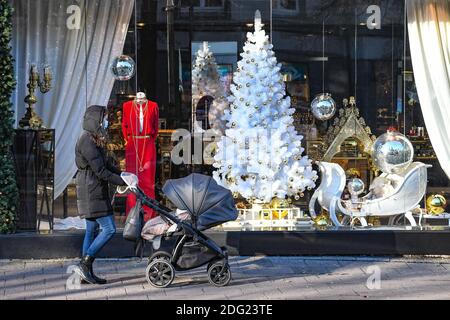 Mädchen mit Kinderwagen zu Fuß in der Stadt in der Nähe eines Geschäfts oder Einkaufszentrum während Covid oder Coronavirus Ausbruch, Weihnachten Hintergrund Stockfoto