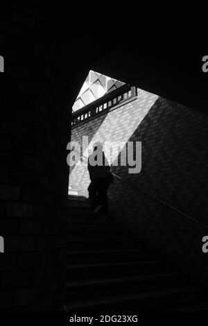 Eine Graustufenaufnahme einer Person, die den Untergrund hochklettert Treppen unter dem Sonnenlicht Stockfoto