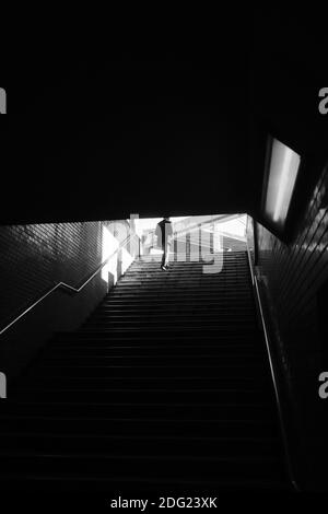 Eine Graustufenaufnahme einer Person, die den Untergrund hochklettert Treppen unter dem Sonnenlicht Stockfoto