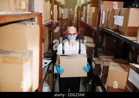 Serious Lagerarbeiter tragen Box, tragen Maske und Handschuhe. Stockfoto