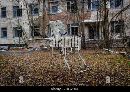 Verlassene gynäkologische Stuhl vor dem Hintergrund eines Krankenhausgebäudes In der verlassenen Stadt pripyat Stockfoto