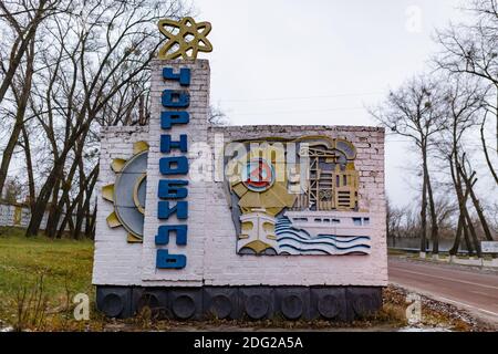 Tschernobyl, Ukraine - August 2019 EIN Schild mit dem Namen Tschernobyl auf Ukrainisch geschrieben. Auf dem Denkmal befindet sich ein gelbes Atom. Auf der Seite Th Stockfoto