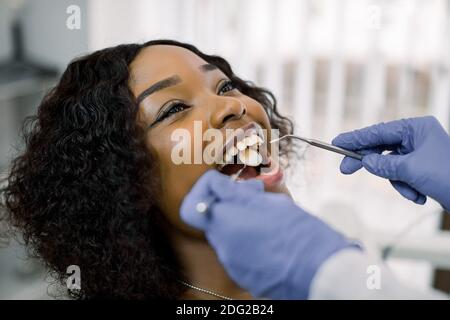 Nahaufnahme Porträt der hübschen jungen afrikanischen Frau Patientin, die zahnärztliche Untersuchung und Behandlung in der Zahnarztpraxis, Blick auf ihren Arzt mit einem Lächeln Stockfoto