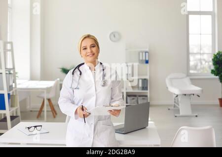Porträt einer stilvollen Ärztin mit Dokumenten in den Händen in der Nähe ihres Arbeitsplatzes. Stockfoto