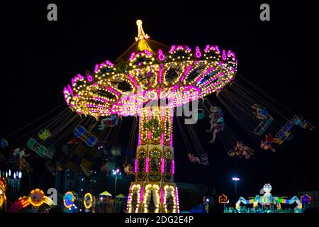 Anapa, Russia - 08/13/2020:Luminous Karussell Plattenspieler drehen mit den Leuten am Abend. Spaß für Kinder und Erwachsene im Vergnügungspark. Verschwommene Bewegung Stockfoto