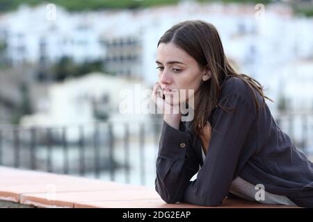 Traurige Frau, die sich beschwert hat, als sie auf einem Balkon in einem hinunterschaute Stadt Stockfoto