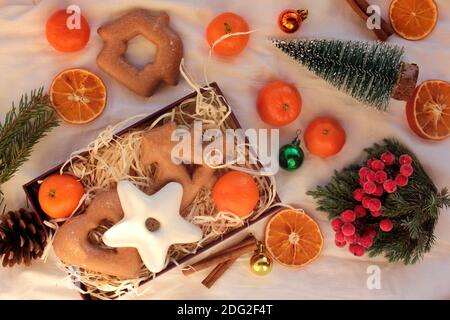 Vorbereitung Winterferien Geschenkbox. Flache Lay-Komposition mit Weihnachts-Lebkuchengebäck, Zitrusfrüchten, Ornamenten und Weihnachtsbaum auf Weiß Stockfoto