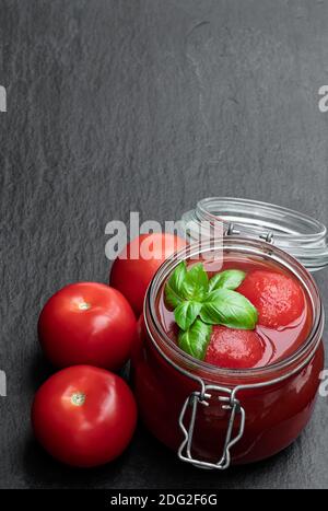 Hausgemachte geschälte Tomaten in Tomatensaft im Glas auf Schwarzer Stein Hintergrund Stockfoto
