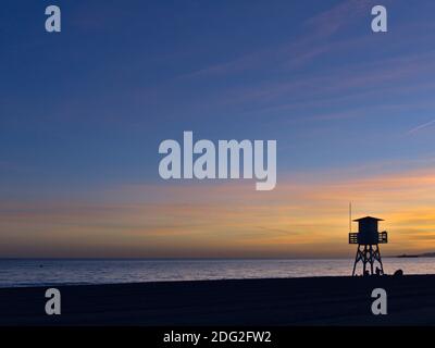 Silhouette bei Sonnenuntergang von einem Wachposten am Strand. Rettungsschwimmer Turm an der Küste Stockfoto