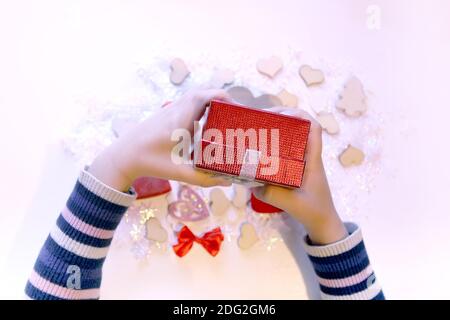 Kleine rote Geschenkbox in Kinderhände. Weihnachten und Neujahr Dekorationen Prozess. Stockfoto